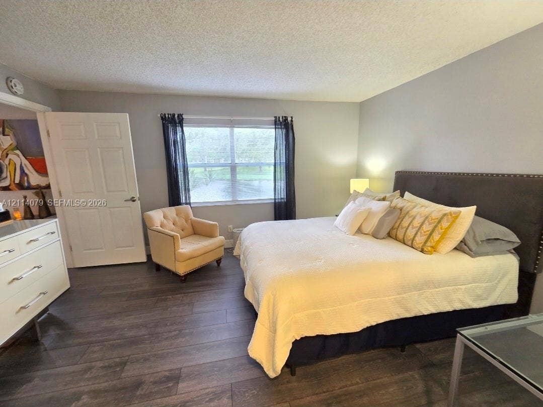 9241 Sunrise Lakes Boulevard, #109, Sunrise, FL 33322 Room featuring wood-finish flooring, a large window, neutral wall paint, and a textured ceiling