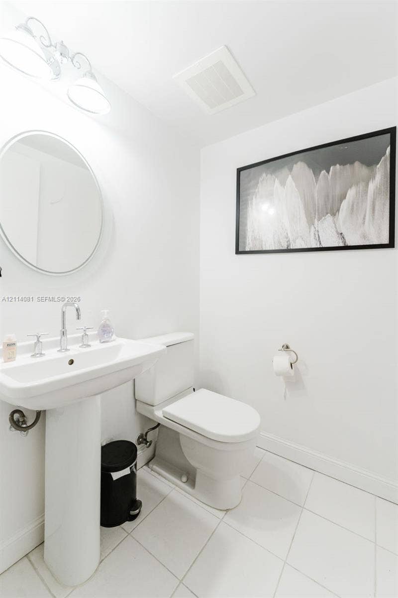 185 SW 7th Street, #3609, Miami, Miami, FL 33130 Pedestal sink featuring a polished chrome faucet, round wall-mounted mirror, ceramic tile flooring, and wall-mounted lighting fixture