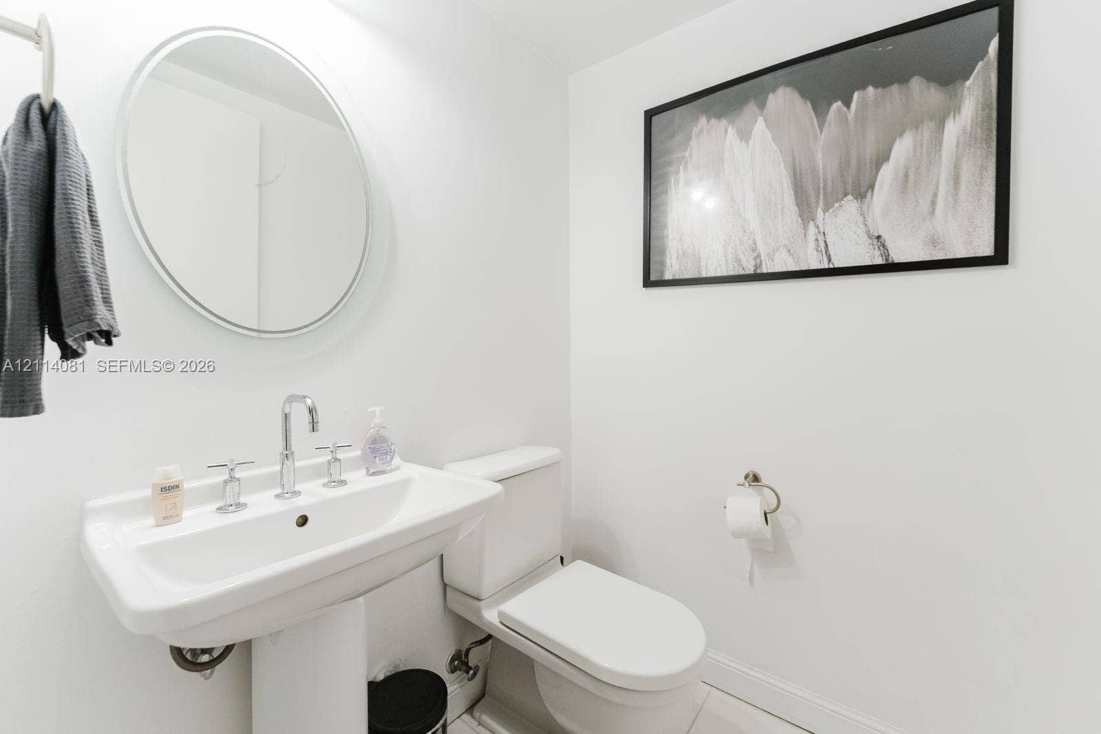 185 SW 7th Street, #3609, Miami, Miami, FL 33130 Pedestal sink with a widespread chrome faucet, oval wall-mounted mirror, and wall-mounted toilet paper holder