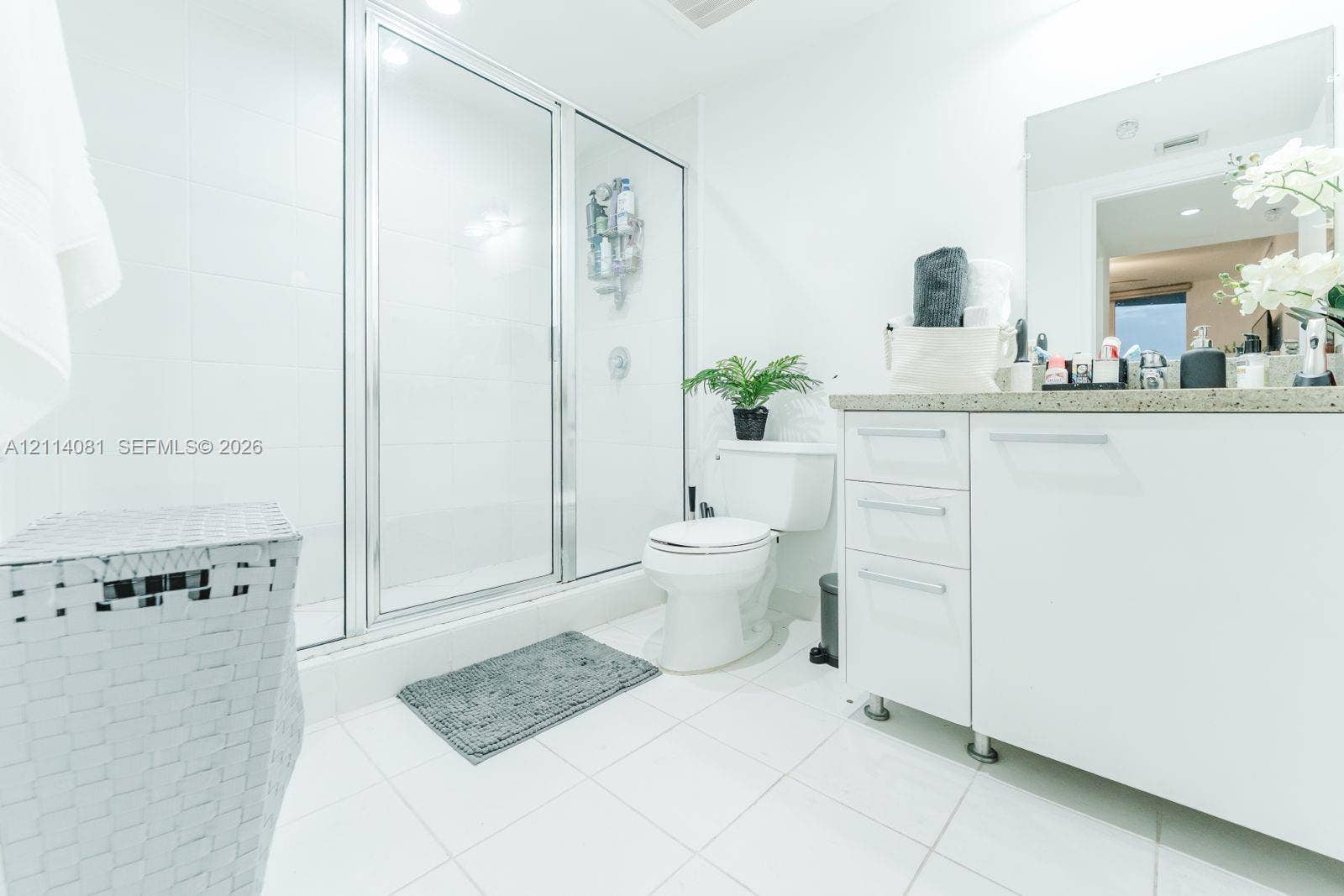 185 SW 7th Street, #3609, Miami, Miami, FL 33130 Bathroom featuring a white vanity with integrated cabinetry, a solid surface countertop, a wall-mounted mirror, and a walk-in shower enclosure with a glass door
