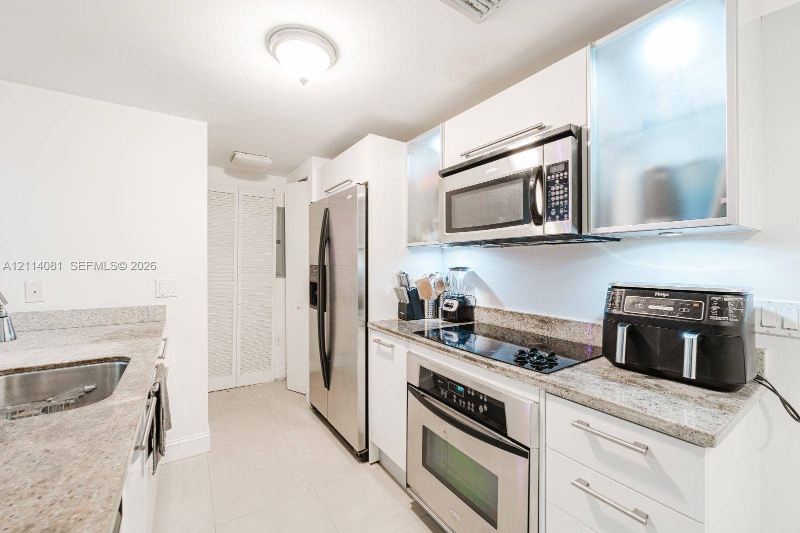 185 SW 7th Street, #3609, Miami, Miami, FL 33130 Kitchen featuring white cabinetry with frosted glass upper panels, stone countertops, stainless steel appliances, and integrated lighting