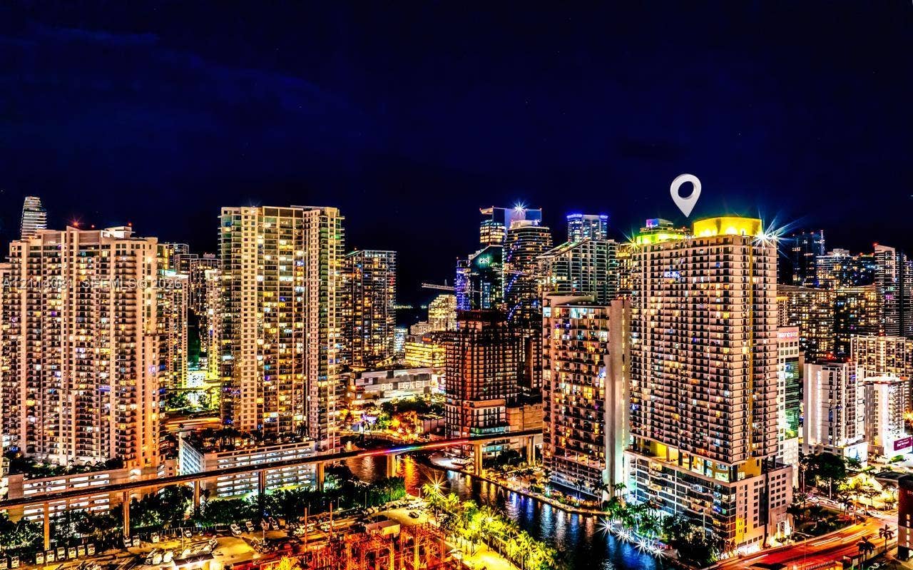 185 SW 7th Street, #3609, Miami, Miami, FL 33130 High-rise residential tower featuring a glass facade, private balconies, an illuminated rooftop structure, and urban waterfront surroundings