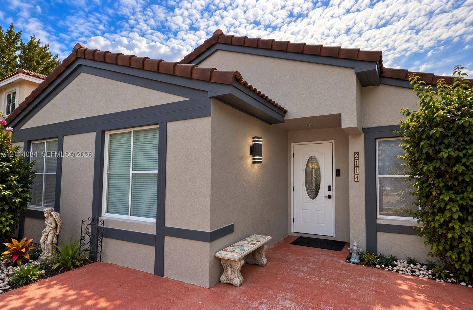 9740 SW 164th Avenue, Miami, FL 33196 Stucco exterior featuring dark-toned trim, a terracotta tile roof, a central entryway with an oval-glass paneled door, and modern cylinder-style wall-mounted lighting
