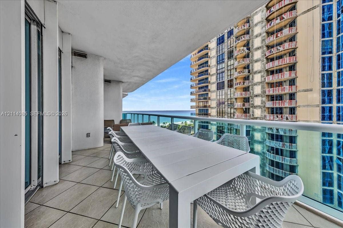 10101 Collins Avenue, #8D, Bal Harbour, FL 33154 Covered balcony featuring oversized neutral floor tiles and a glass-paneled railing overlooking the ocean