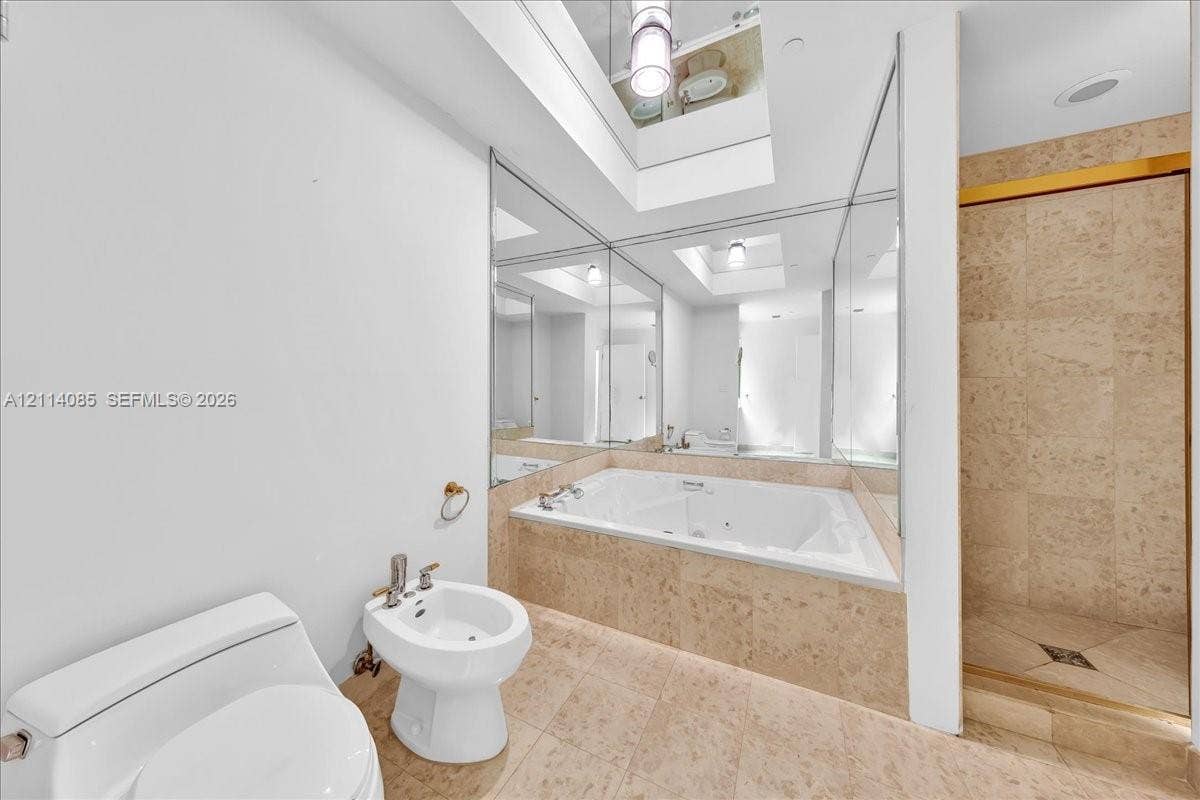 10101 Collins Avenue, #8D, Bal Harbour, FL 33154 Jetted soaking tub with tile surround, walk-in shower with tile walls, bidet, and floor-to-ceiling mirrored walls featuring a skylight