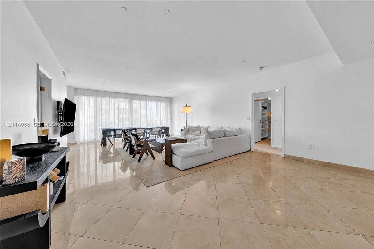 10101 Collins Avenue, #8D, Bal Harbour, FL 33154 Open-concept living space featuring high ceilings, polished stone-finish tile flooring, and floor-to-ceiling windows with integrated drapery tracks