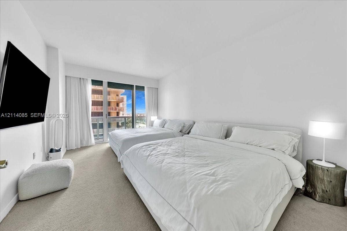 10101 Collins Avenue, #8D, Bal Harbour, FL 33154 Floor-to-ceiling glass sliding doors opening to a private balcony, wall-mounted television, neutral carpeting, and smooth white wall finishes