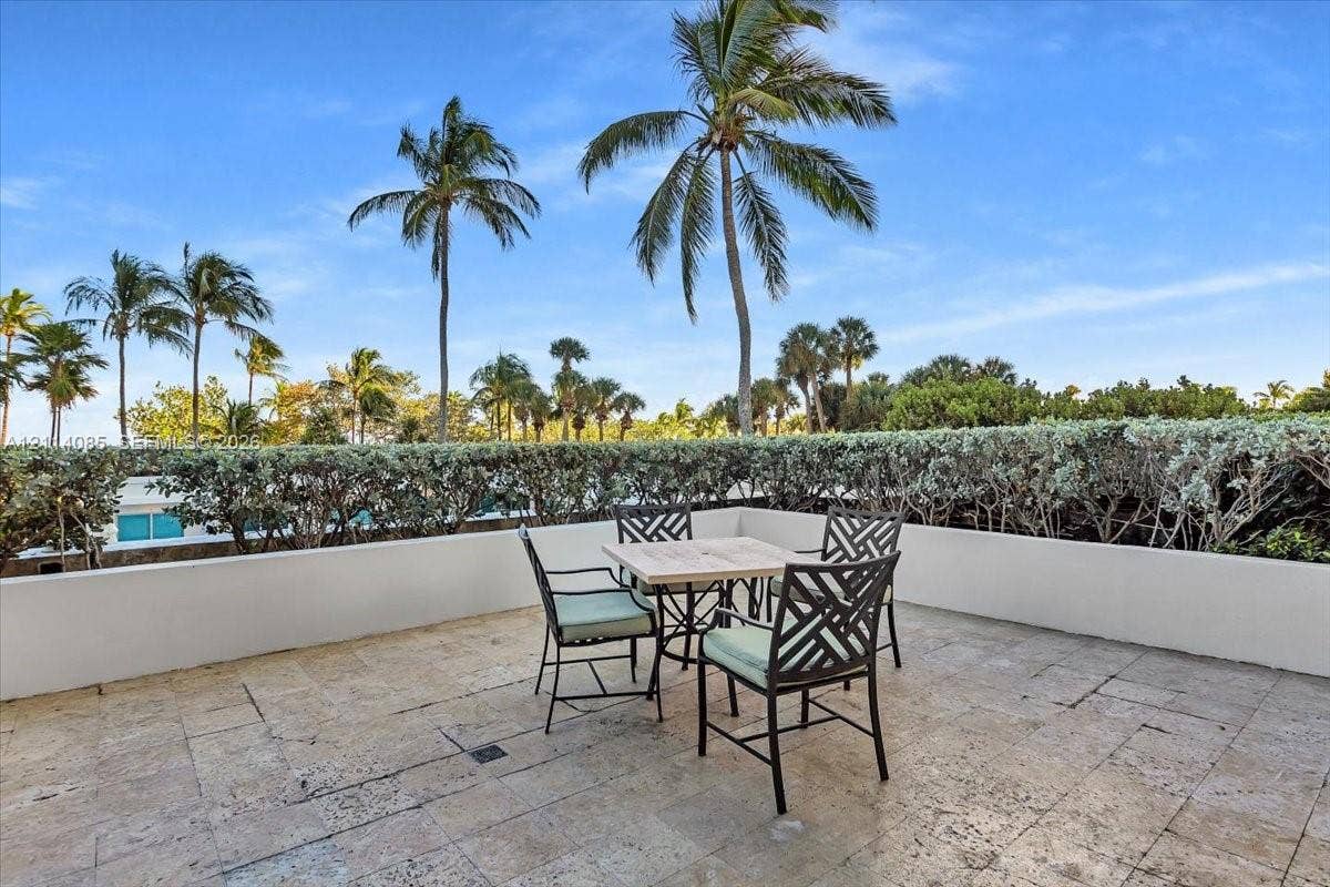 10101 Collins Avenue, #8D, Bal Harbour, FL 33154 Elevated terrace featuring natural stone flooring, low-profile concrete perimeter walls, and manicured hedge screening with palm trees