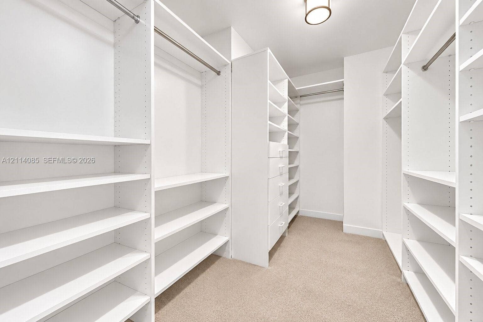 10101 Collins Avenue, #8D, Bal Harbour, FL 33154 Walk-in closet featuring white custom built-in shelving, integrated hanging rods, a column of pull-out drawers, and neutral carpeting