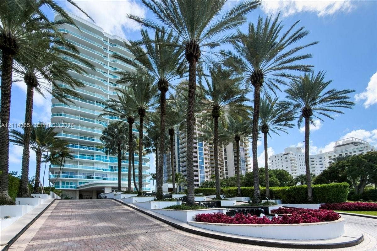 10101 Collins Avenue, #8D, Bal Harbour, FL 33154 High-rise residential exterior featuring a paved drive, mature palm tree landscaping, tiered concrete planters, and integrated greenery