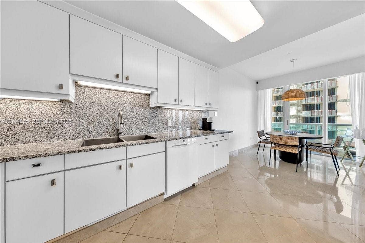10101 Collins Avenue, #8D, Bal Harbour, FL 33154 Kitchen featuring white cabinetry, stone-flecked countertops, full-height backsplash, polished tile flooring, and integrated dishwasher