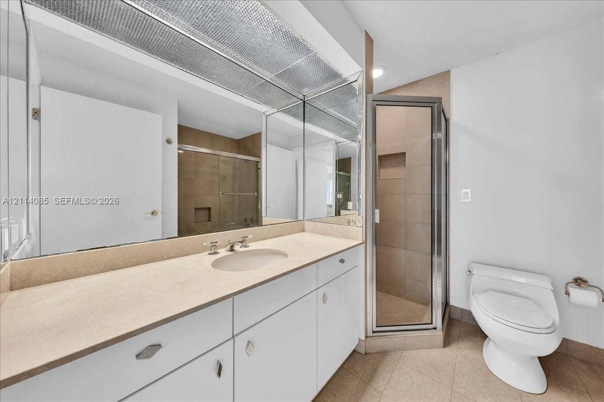 10101 Collins Avenue, #8D, Bal Harbour, FL 33154 Bathroom featuring white cabinetry, solid-surface countertop, full-width mirror, and a glass-enclosed shower with tile surround