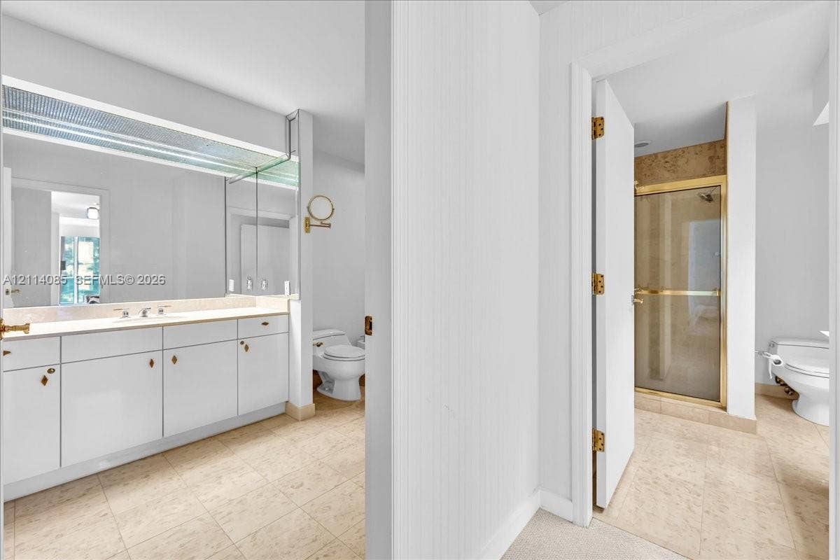 10101 Collins Avenue, #8D, Bal Harbour, FL 33154 Bathroom featuring white cabinetry, full-width mirror, stone-finish flooring, glass-enclosed shower, and built-in vanity lighting