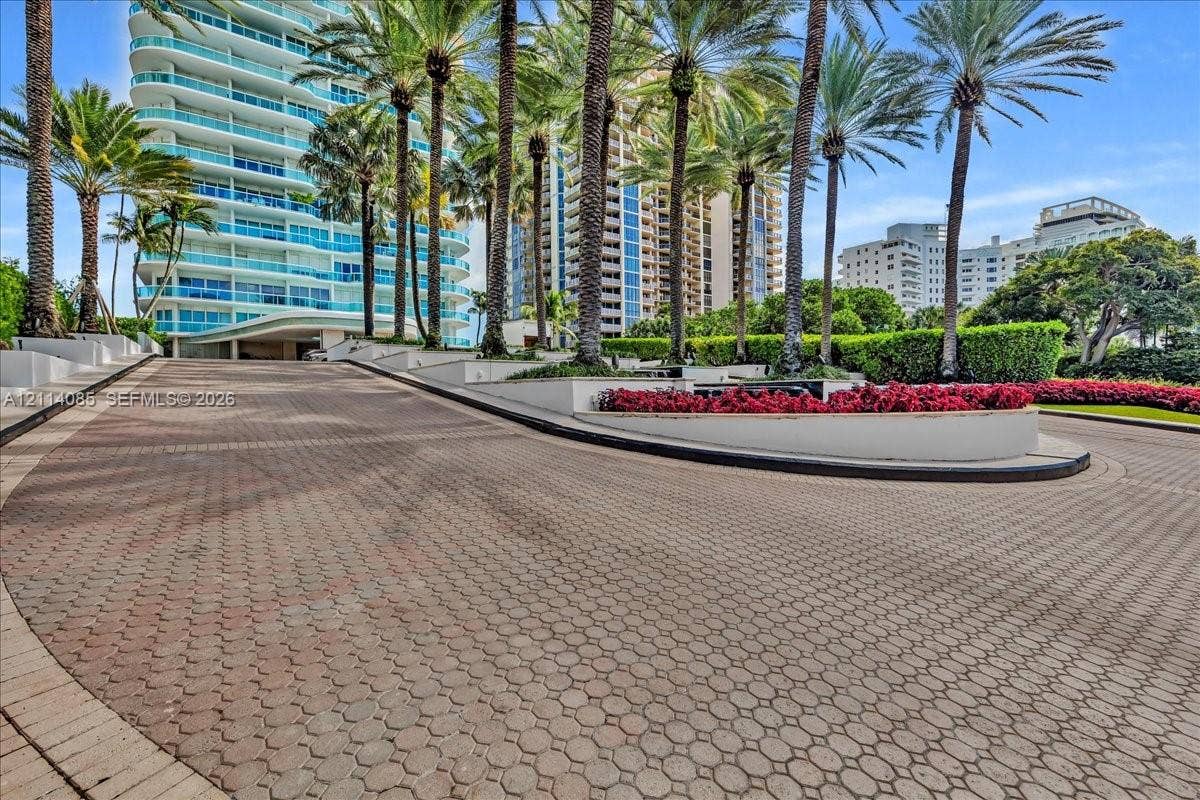 10101 Collins Avenue, #8D, Bal Harbour, FL 33154 Paver stone driveway featuring manicured perimeter landscaping, elevated concrete planters, and mature palm trees