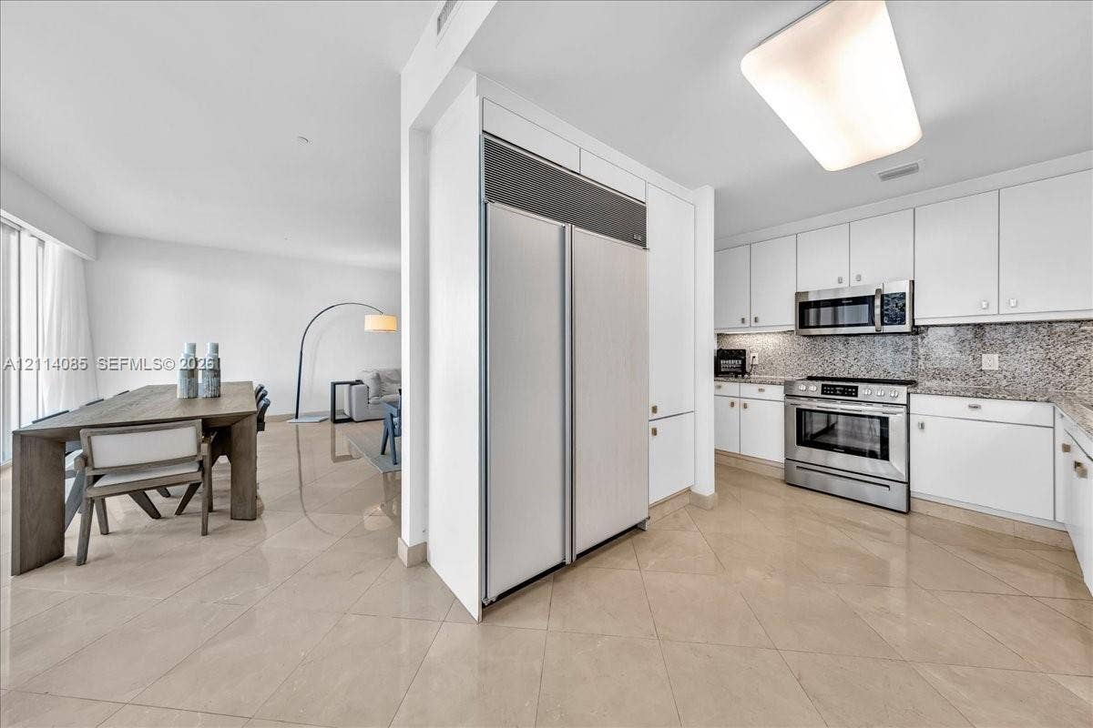 10101 Collins Avenue, #8D, Bal Harbour, FL 33154 Kitchen featuring white cabinetry, stone countertops, stainless steel appliances, and large-format tile flooring