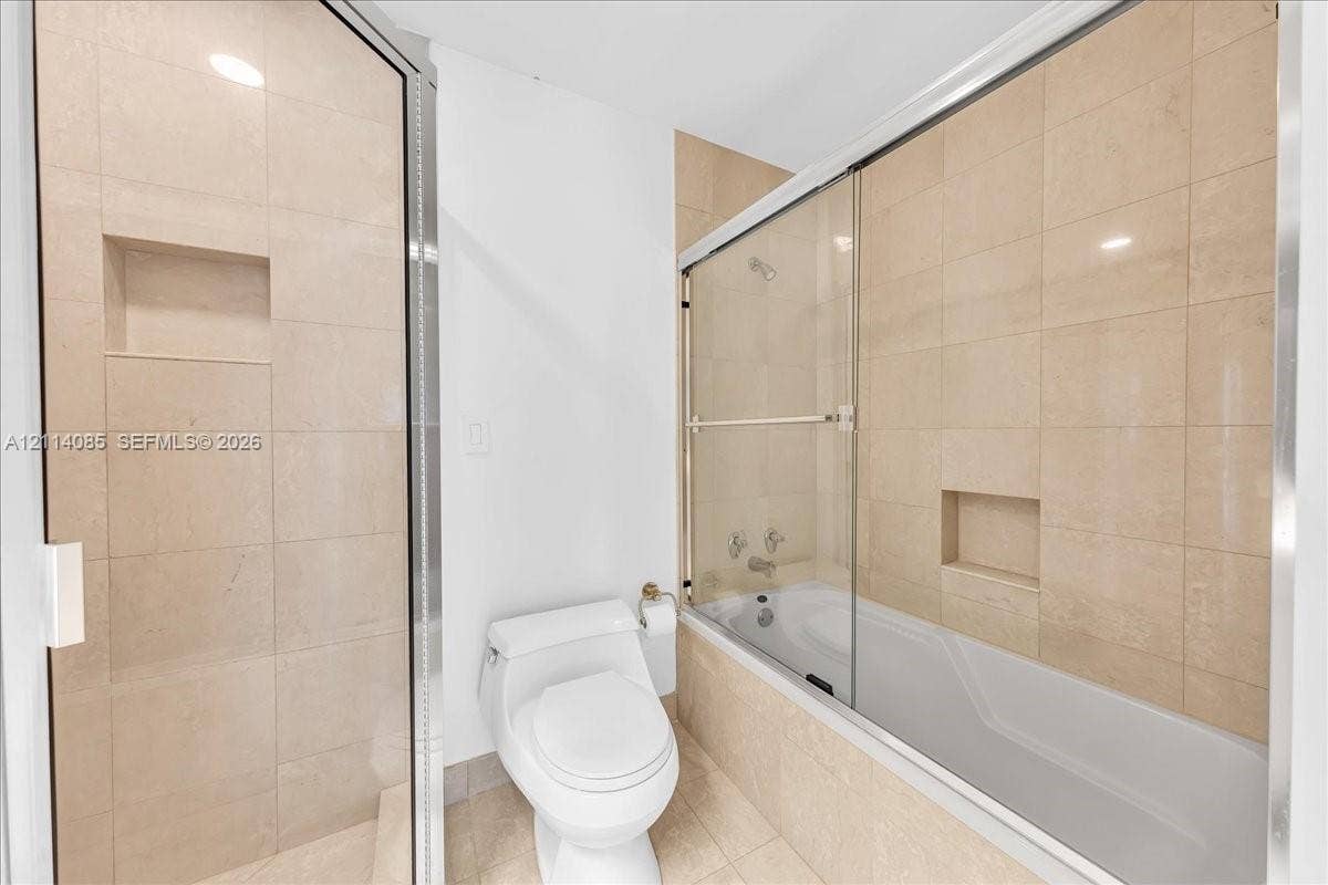 10101 Collins Avenue, #8D, Bal Harbour, FL 33154 Neutral-toned tile surrounds in the shower and tub enclosure, glass sliding shower doors, built-in tile wall niches, and a white porcelain toilet