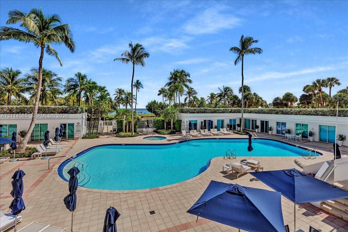 10101 Collins Avenue, #8D, Bal Harbour, FL 33154 Outdoor recreation area featuring a large swimming pool, integrated spa, tiled pool deck, and mature palm trees