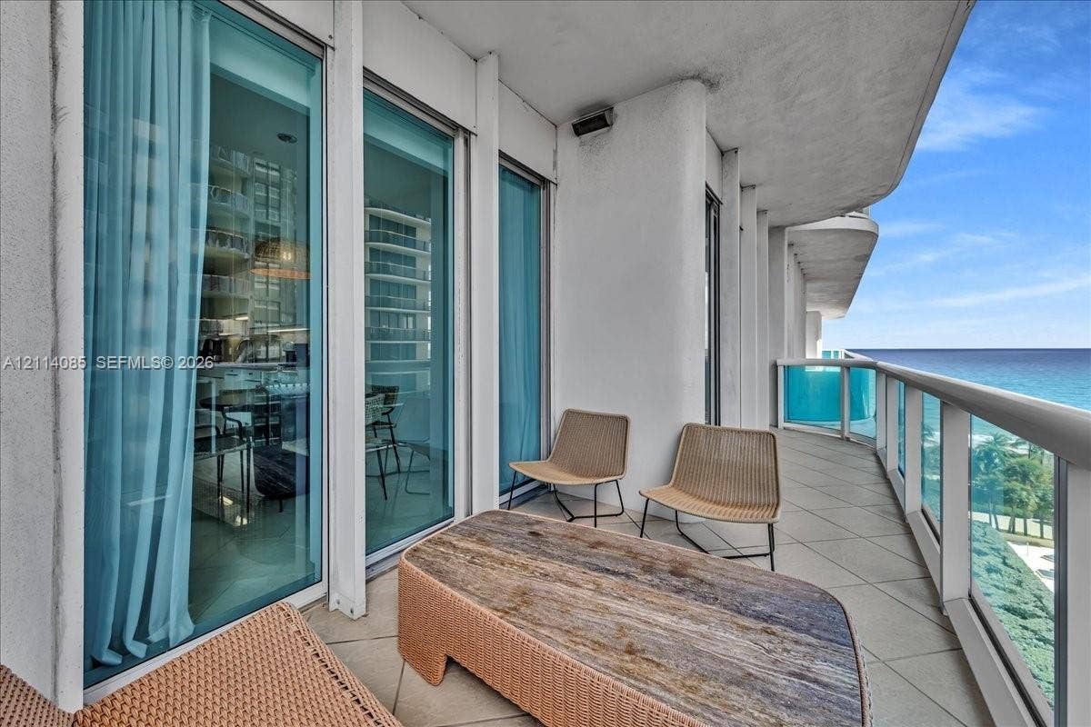 10101 Collins Avenue, #8D, Bal Harbour, FL 33154 Spacious covered balcony with large-format tile flooring, floor-to-ceiling glass sliding doors, and a glass-paneled railing overlooking the ocean