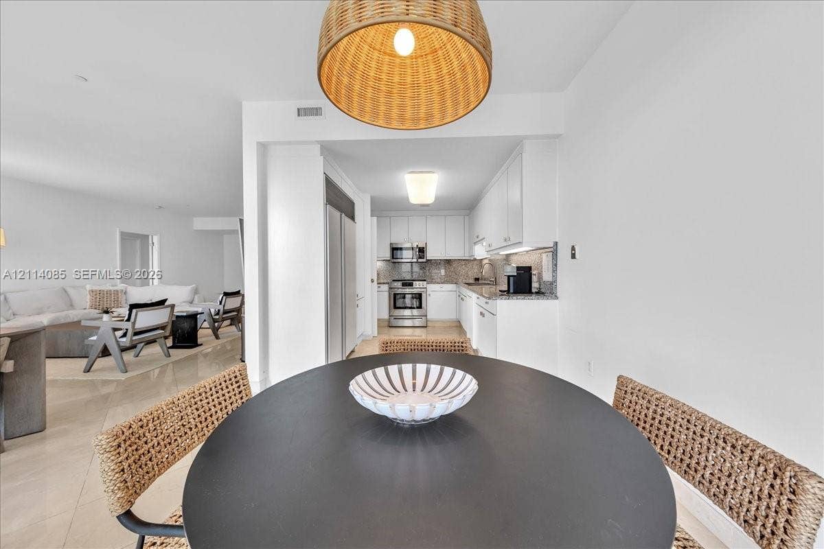 10101 Collins Avenue, #8D, Bal Harbour, FL 33154 Kitchen featuring stainless steel appliances, white cabinetry, solid surface countertops, tile backsplash, and oversized dome pendant lighting