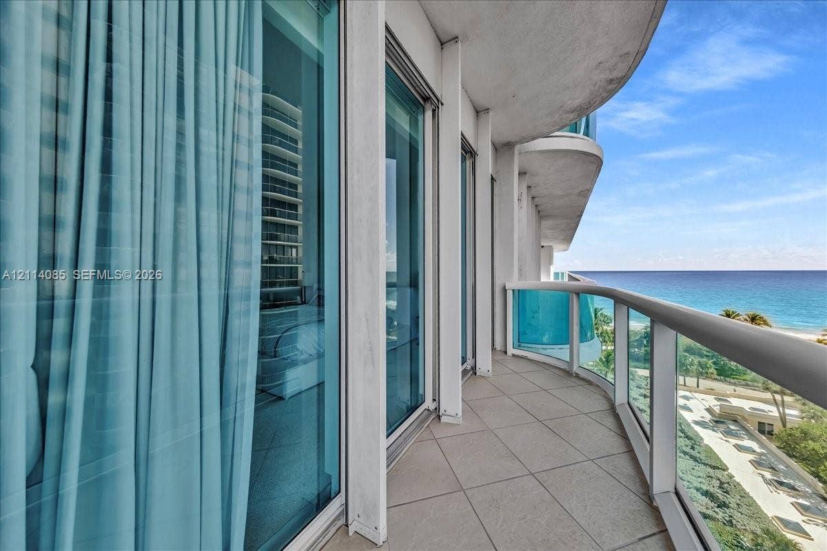 10101 Collins Avenue, #8D, Bal Harbour, FL 33154 Curved private balcony featuring large-format tile flooring, glass panel railings, and floor-to-ceiling sliding glass doors
