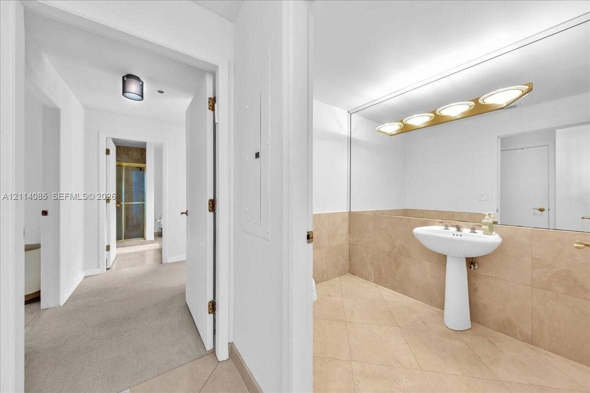 10101 Collins Avenue, #8D, Bal Harbour, FL 33154 Bathroom featuring a pedestal sink, large vanity mirror with multi-bulb light fixture, beige tile flooring, and tile wall wainscoting