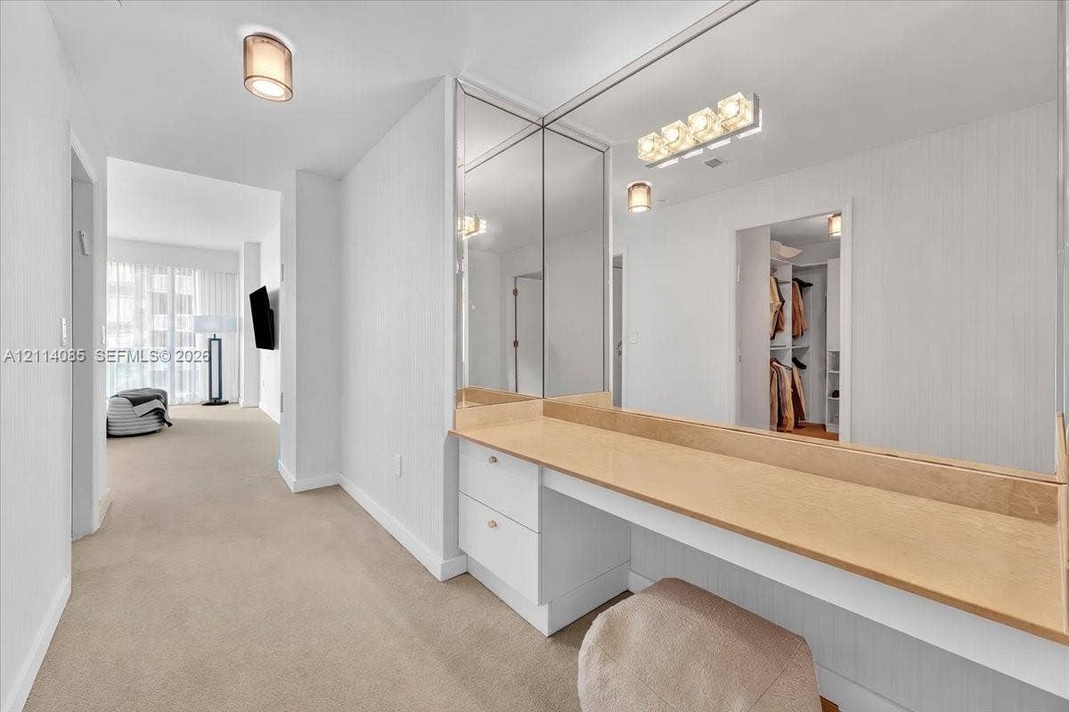 10101 Collins Avenue, #8D, Bal Harbour, FL 33154 Built-in vanity featuring a light-toned countertop, white cabinetry with drawer storage, full-length mirror paneling, and wall-mounted light fixtures