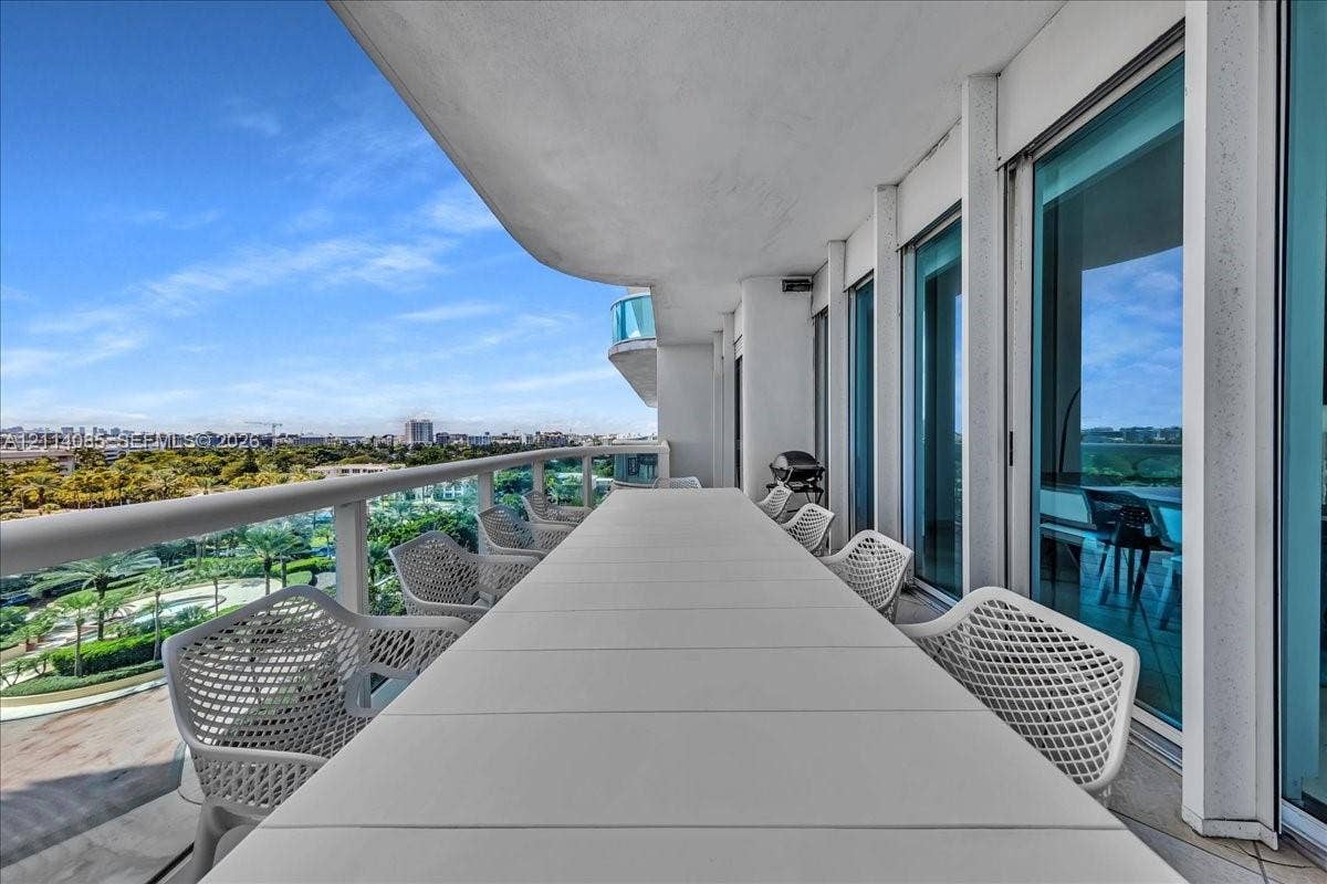10101 Collins Avenue, #8D, Bal Harbour, FL 33154 Covered balcony featuring a wrap-around glass railing and tile flooring, accessible via floor-to-ceiling sliding glass doors