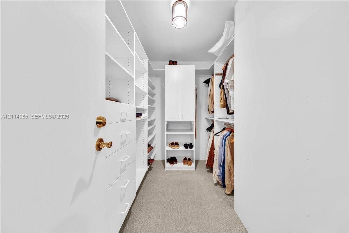 10101 Collins Avenue, #8D, Bal Harbour, FL 33154 Walk-in storage space featuring built-in white cabinetry, multiple shelving units, integrated drawer storage, and overhead pendant lighting