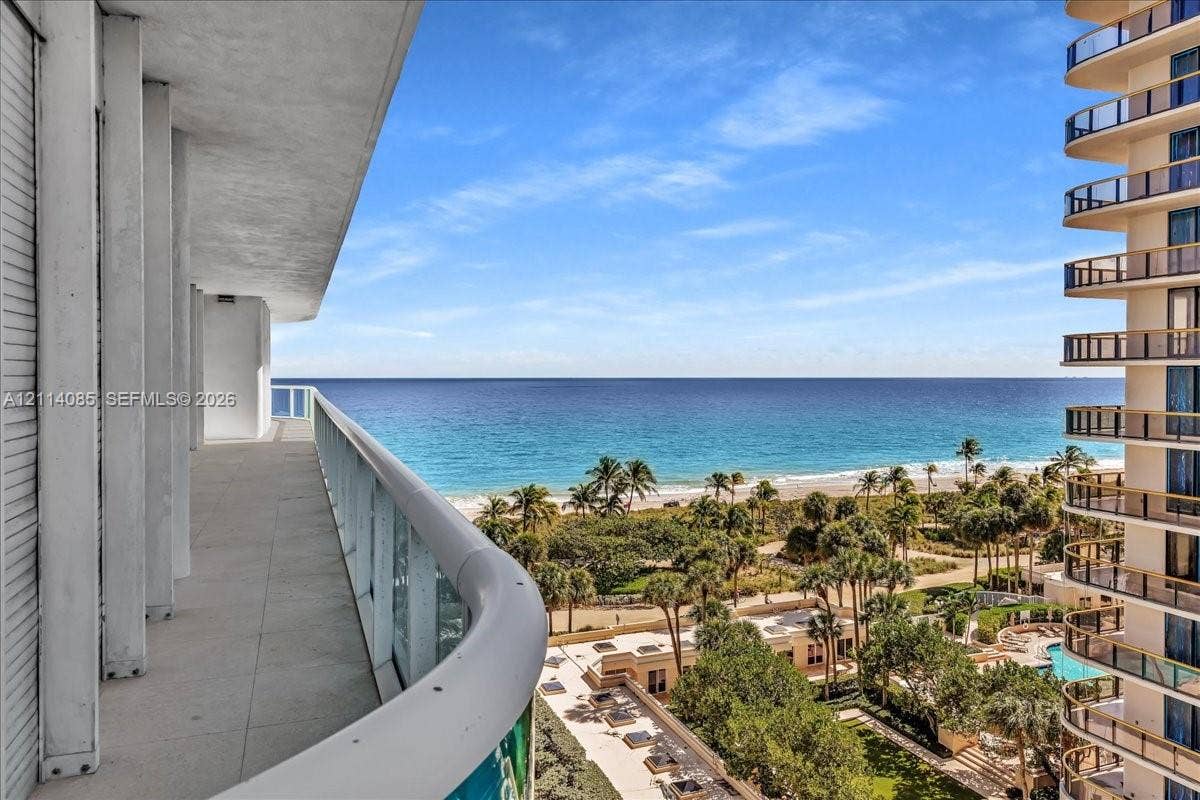10101 Collins Avenue, #8D, Bal Harbour, FL 33154 Expansive covered balcony featuring tile flooring and a glass railing, overlooking the coastline and ocean horizon