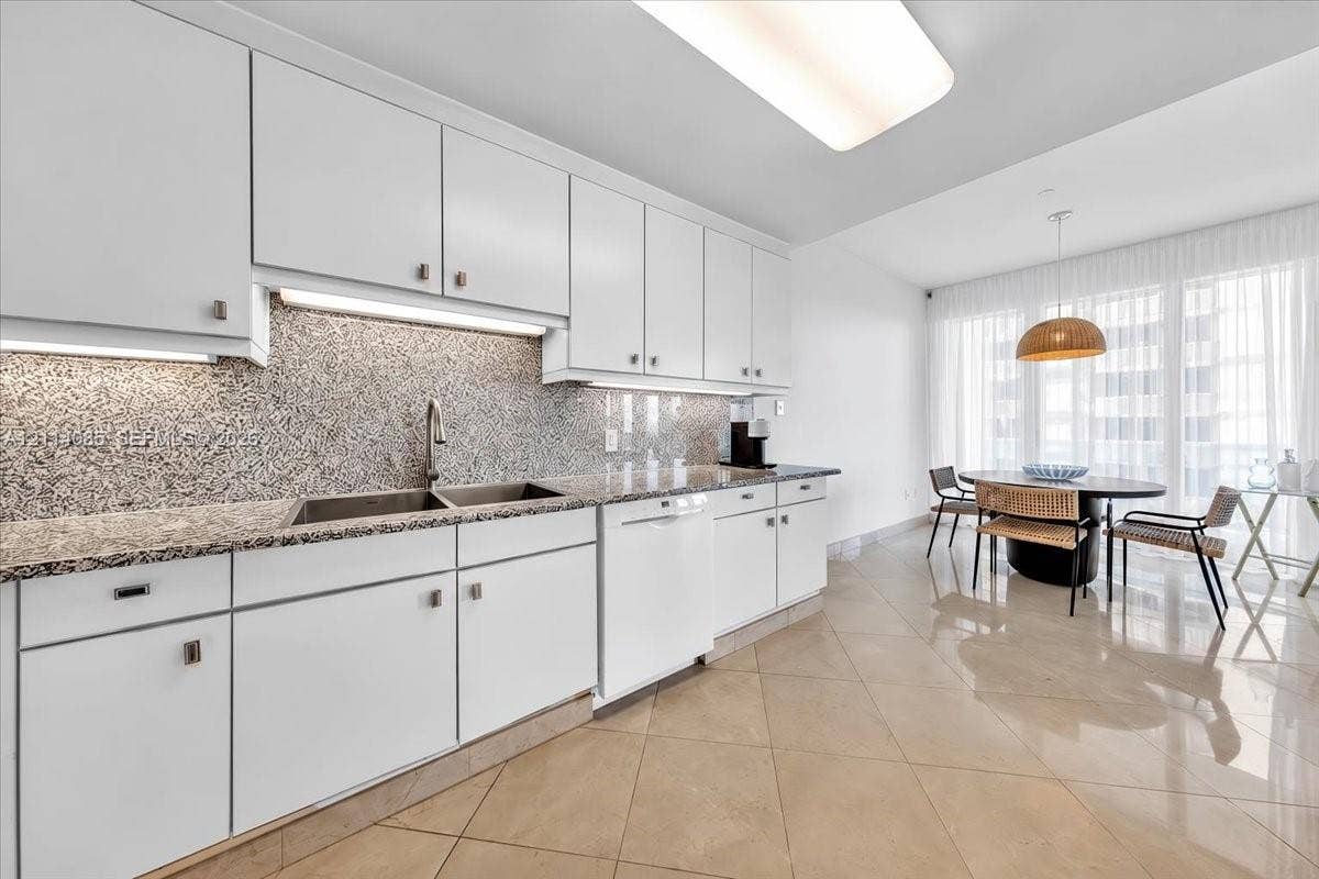 10101 Collins Avenue, #8D, Bal Harbour, FL 33154 Kitchen featuring white cabinetry, stone-finish countertops, full-height stone-finish backsplash, stainless steel dual-basin sink, and polished tile flooring