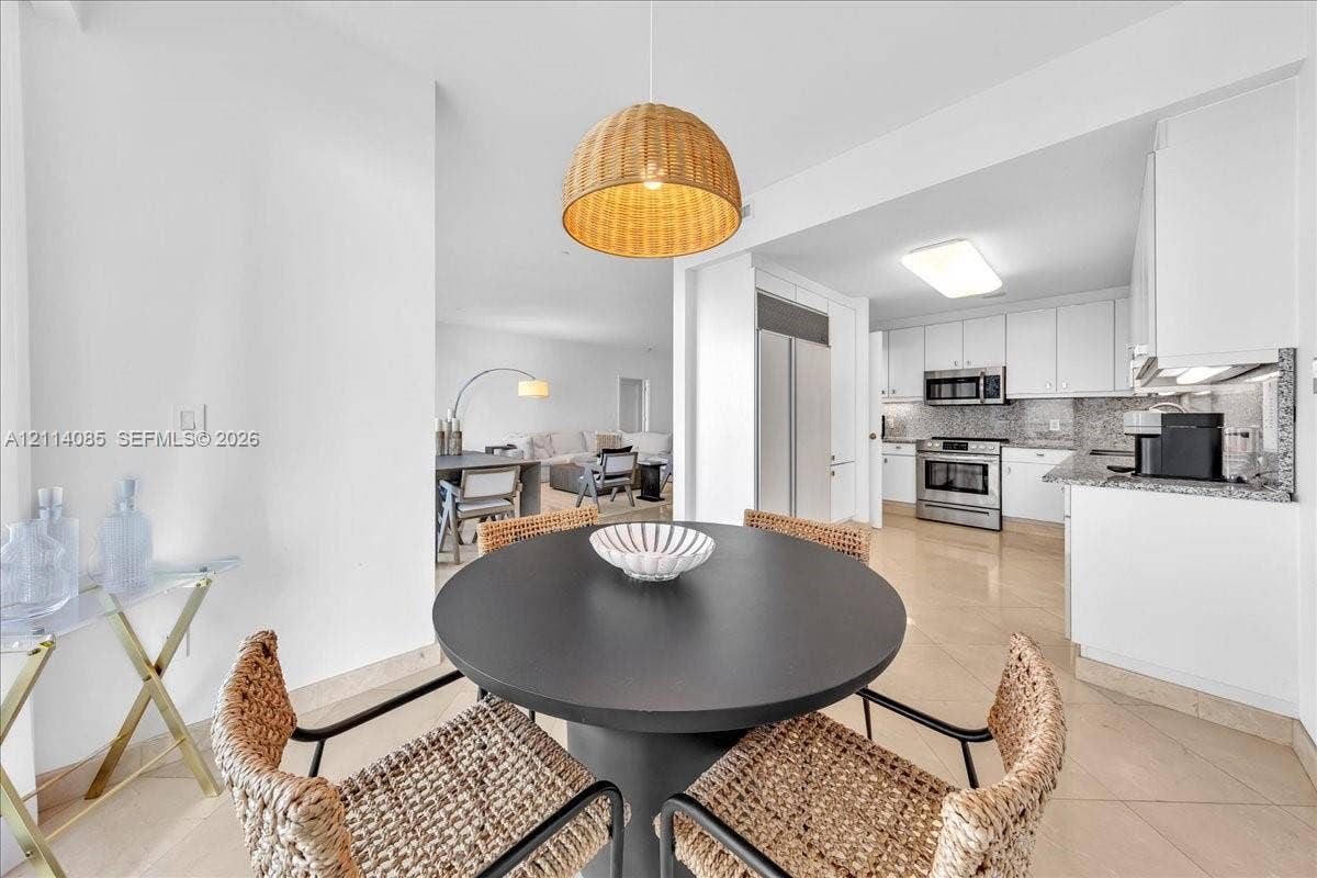 10101 Collins Avenue, #8D, Bal Harbour, FL 33154 Kitchen featuring white cabinetry, stone countertops, and stainless steel appliances, complemented by large-format tile flooring and a woven pendant light fixture