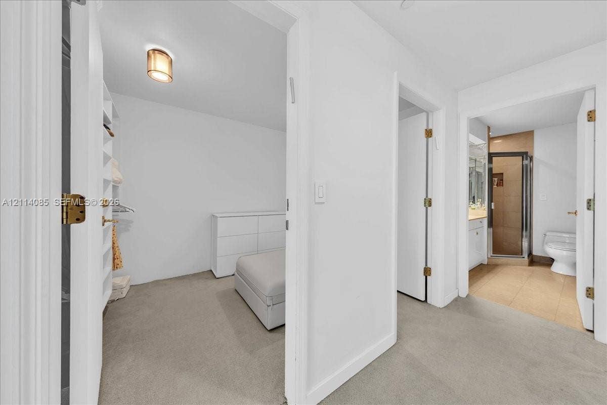 10101 Collins Avenue, #8D, Bal Harbour, FL 33154 Walk-in closet featuring built-in shelving, flush-mount lighting, and neutral carpeting, with a separate bathroom showcasing a glass-enclosed shower and tile flooring