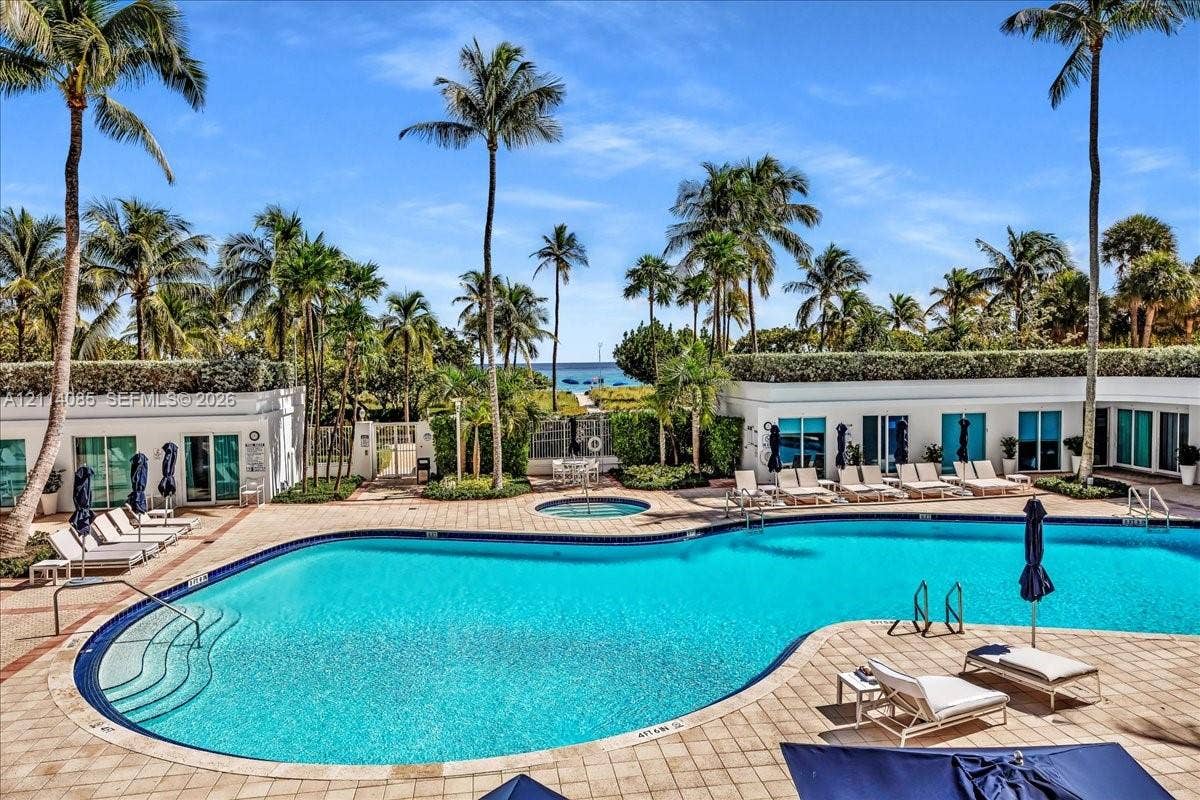 10101 Collins Avenue, #8D, Bal Harbour, FL 33154 Resort-style pool area featuring a curved swimming pool, integrated spa, paved terrace, and mature palm trees