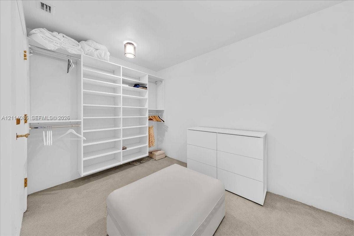 10101 Collins Avenue, #8D, Bal Harbour, FL 33154 Walk-in closet featuring white custom built-in shelving, hanging rods, and neutral carpeting