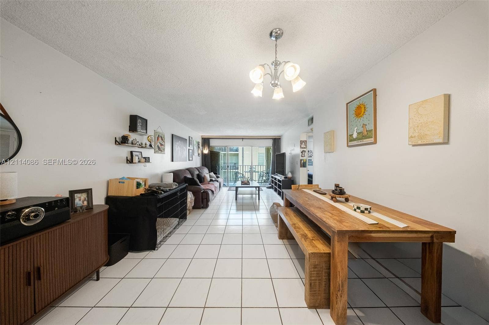 706 NW 87th Avenue, #204, Miami, Miami, FL 33172 Open-concept interior featuring large-format ceramic tile flooring, a multi-arm polished metal chandelier, and a sliding glass door providing access to a private balcony