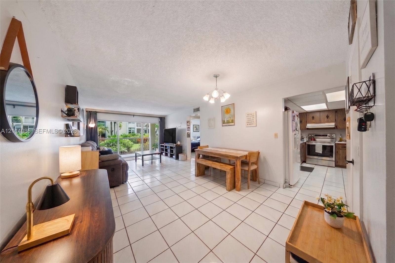 706 NW 87th Avenue, #204, Miami, Miami, FL 33172 Open floor plan featuring large format ceramic tile flooring, multi-arm chandelier lighting, sliding glass balcony doors, and kitchen cabinetry with integrated appliance housing