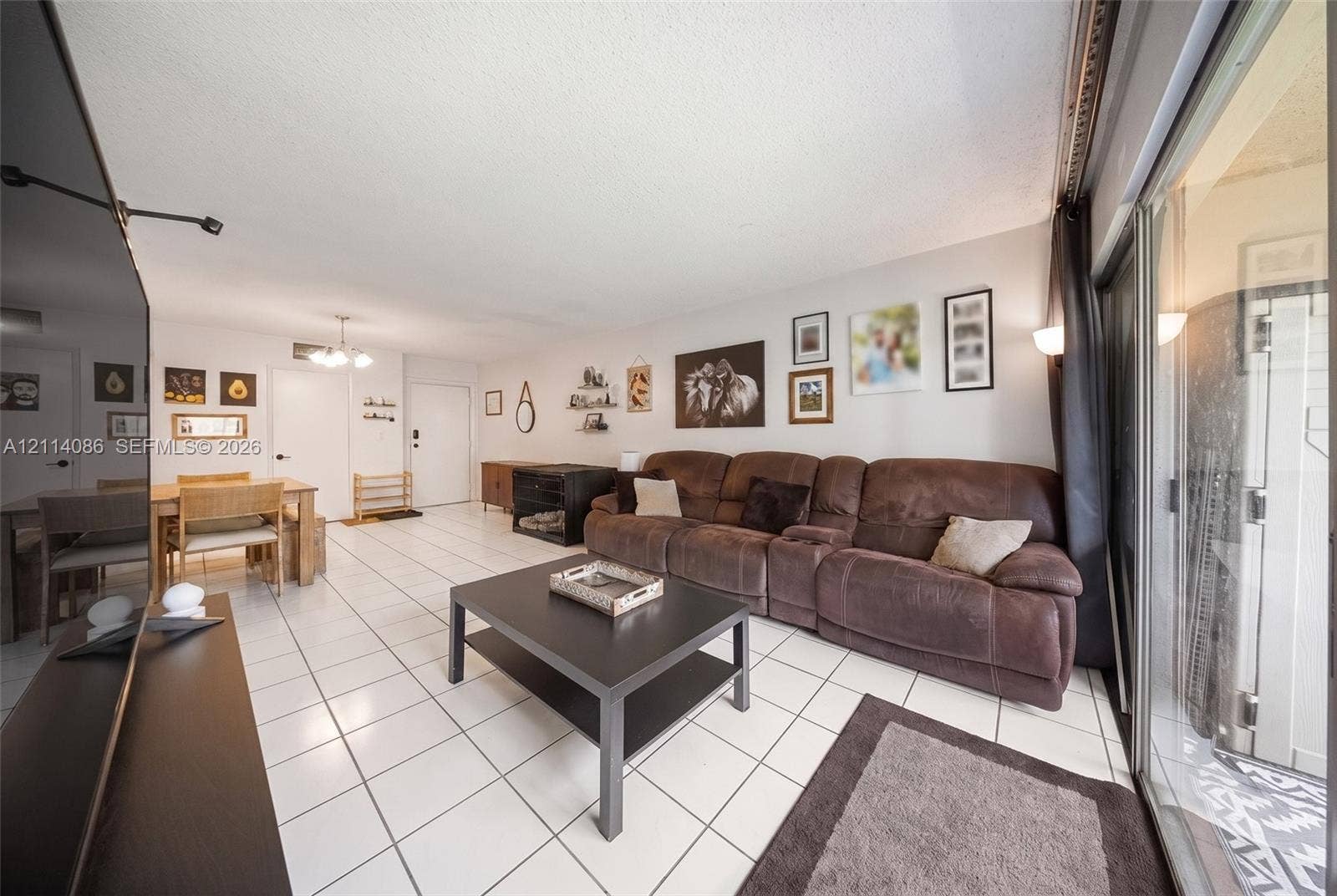706 NW 87th Avenue, #204, Miami, Miami, FL 33172 Open-concept interior featuring large-format ceramic tile flooring, sliding glass patio doors, and a multi-arm ceiling light fixture