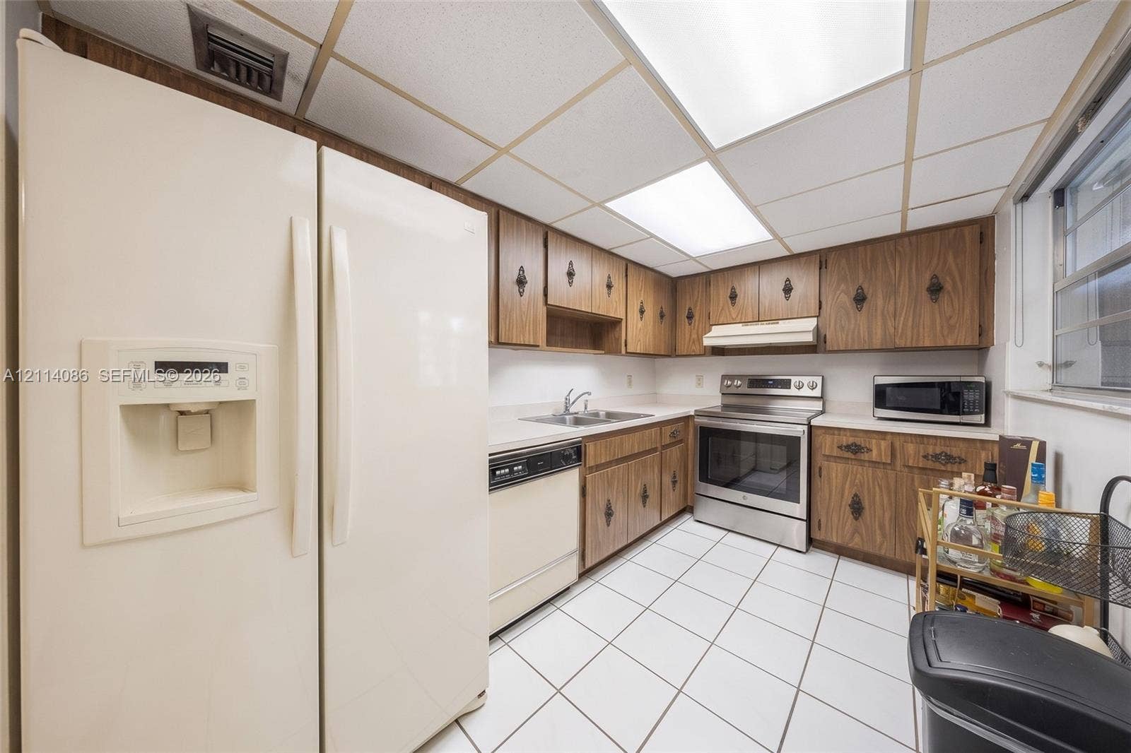 706 NW 87th Avenue, #204, Miami, Miami, FL 33172 Kitchen featuring wood-finish cabinetry, stainless steel range, white tile flooring, drop ceiling panels, and ample solid-surface countertops