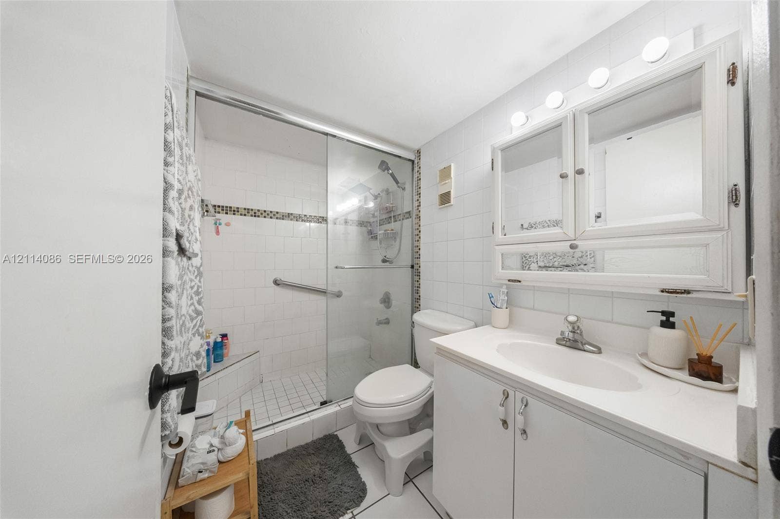 706 NW 87th Avenue, #204, Miami, Miami, FL 33172 Bathroom featuring a vanity with white cabinetry, a surface-mounted medicine cabinet, a tiled shower enclosure with a glass door, and wall-mounted light fixtures