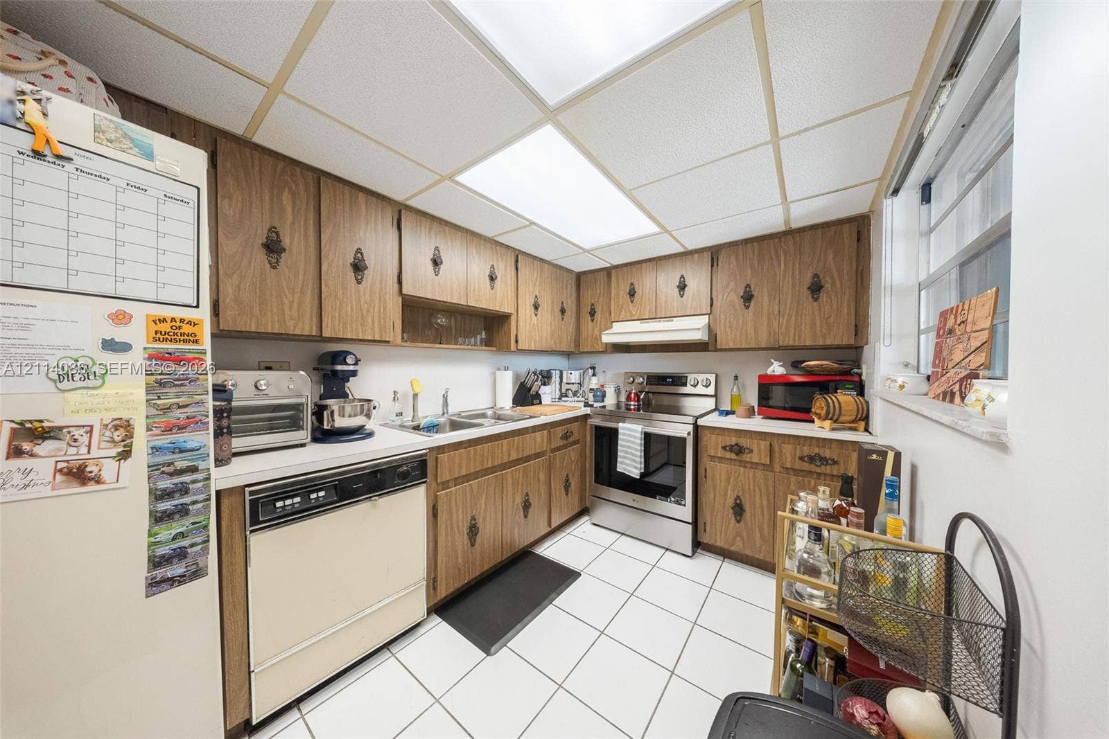 706 NW 87th Avenue, #204, Miami, Miami, FL 33172 Kitchen featuring wood-finish cabinetry with ornate hardware, stainless steel slide-in range, integrated dishwasher, white tiled flooring, and drop-ceiling panel lighting