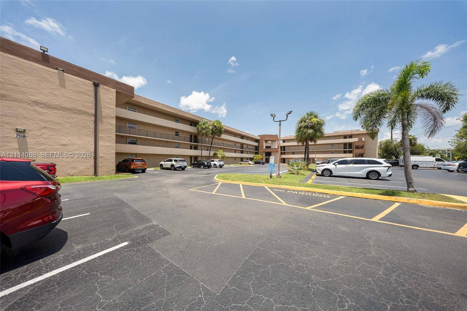 706 NW 87th Avenue, #204, Miami, Miami, FL 33172 Multi-story exterior featuring a stucco facade, covered balconies, asphalt parking area, and mature palm trees