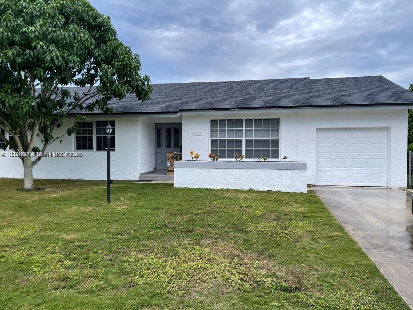 17220 SW 93rd Avenue, #0, Palmetto Bay, Palmetto Bay, FL 33157 Single-story exterior featuring a white stucco facade, shingled roof, attached one-car garage, multi-pane windows, and a front masonry planter