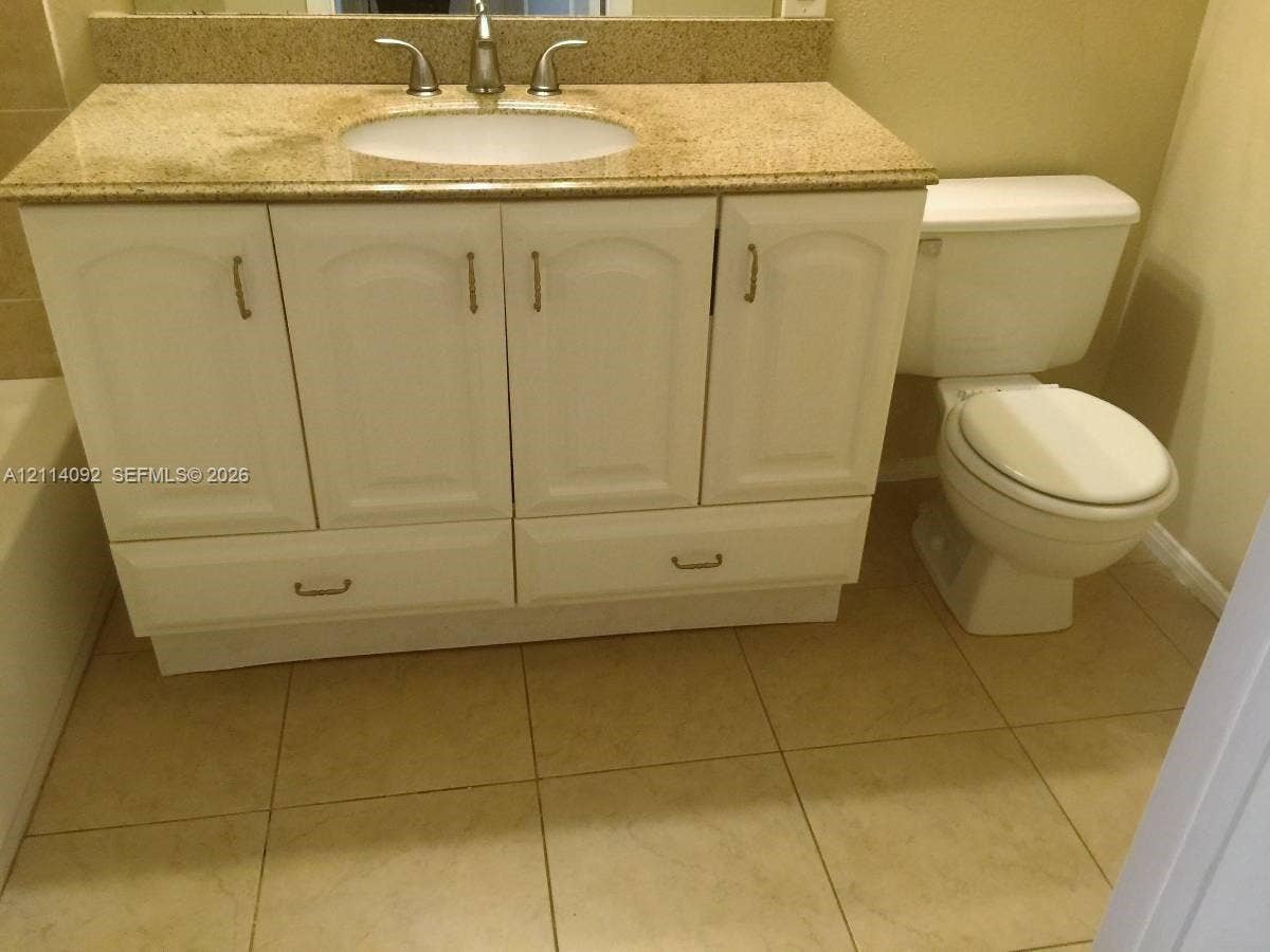 2667 NW 33rd Street, #2413, Oakland Park, Oakland Park, FL 33309 Vanity cabinet with white-finish cabinetry and stone-composite countertop, undermount sink with metal faucet, and ceramic tile flooring
