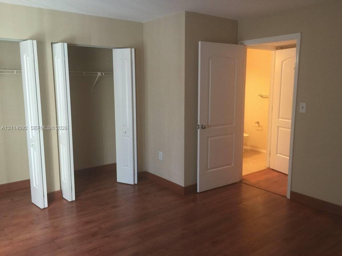 2667 NW 33rd Street, #2413, Oakland Park, Oakland Park, FL 33309 Room featuring wood-finish flooring, two sets of bifold closet doors with built-in shelving, and two interior doors with molded panel detailing