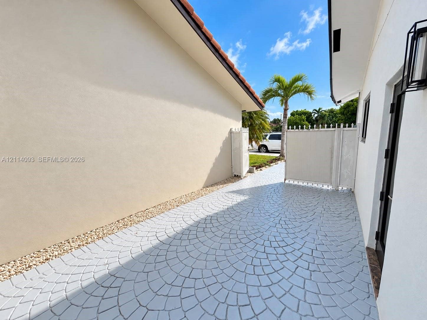 4916 SW 142nd Place, #4916, Miami, Miami, FL 33175 Side exterior featuring stamped concrete patio, light-colored stucco siding, gravel ground cover, and a white privacy gate