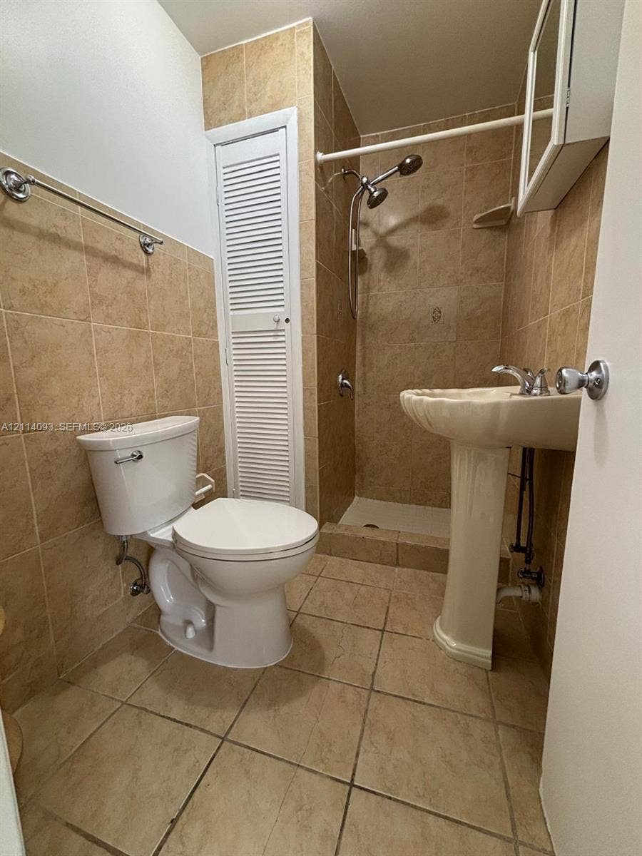 4916 SW 142nd Place, #4916, Miami, Miami, FL 33175 Bathroom featuring a pedestal sink, a walk-in shower with tile surround, full-wall tile backsplash, and built-in closet with louvered doors