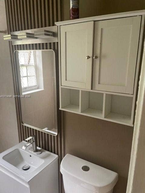 14180 NW 22nd Court, #0, Opa Locka, Opa Locka, FL 33054 Bathroom vanity featuring a rectangular basin and single-handle faucet, wall-mounted rectangular mirror, tiered linear light fixture, white dual-door wall cabinet with open shelving, and porcelain toilet