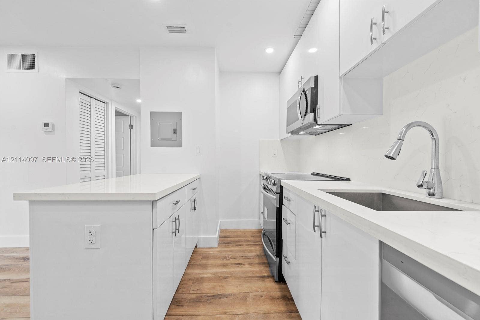 7905 SW 104th Street, #206H, Miami, FL 33156 Kitchen featuring high-gloss white cabinetry, quartz countertops, a stainless steel under-mount sink with a gooseneck faucet, stainless steel appliances, and wood-finish flooring