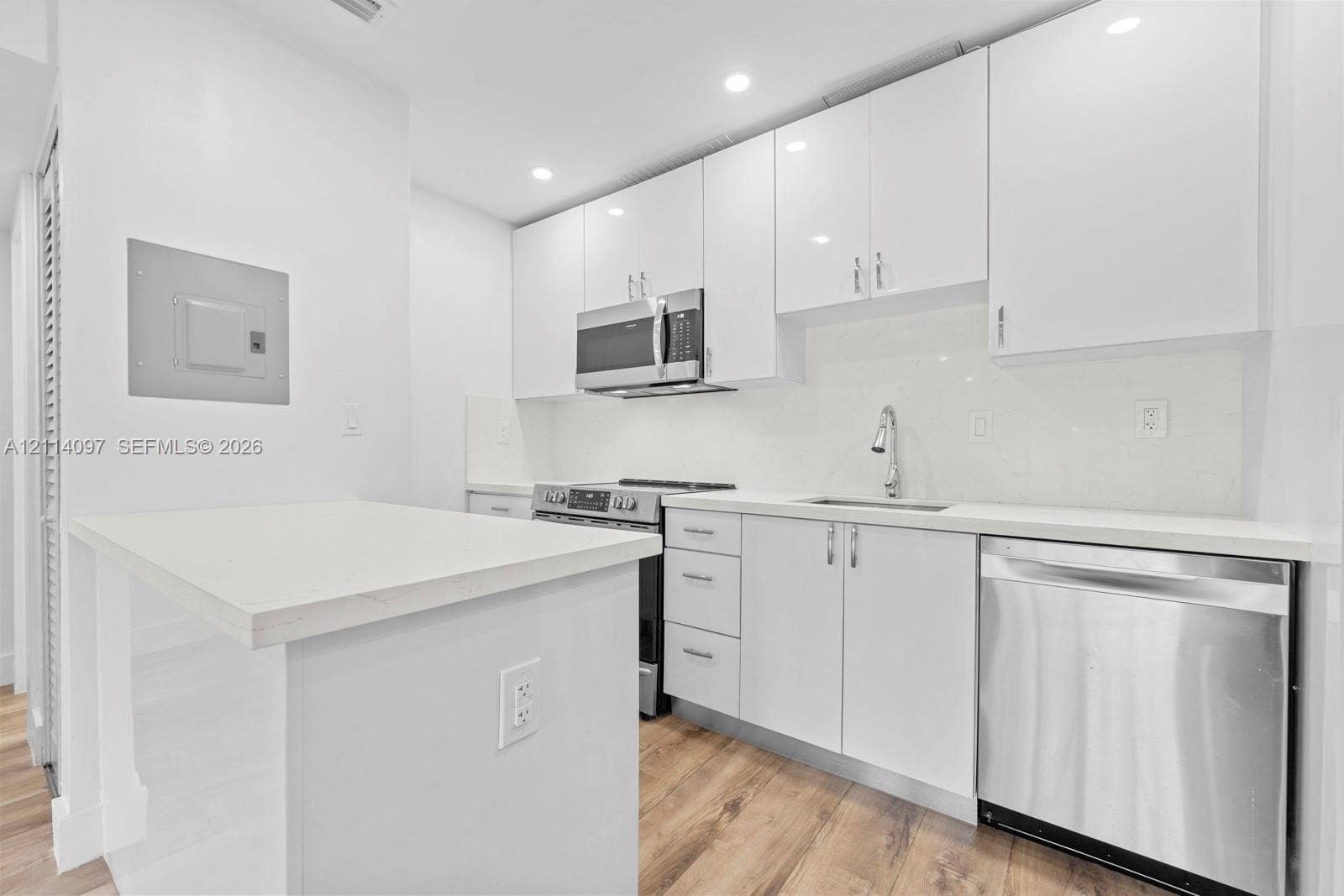 7905 SW 104th Street, #206H, Miami, FL 33156 Kitchen featuring white high-gloss cabinetry, stainless steel appliances, white solid-surface countertops, wood-finish flooring, and recessed ceiling lighting