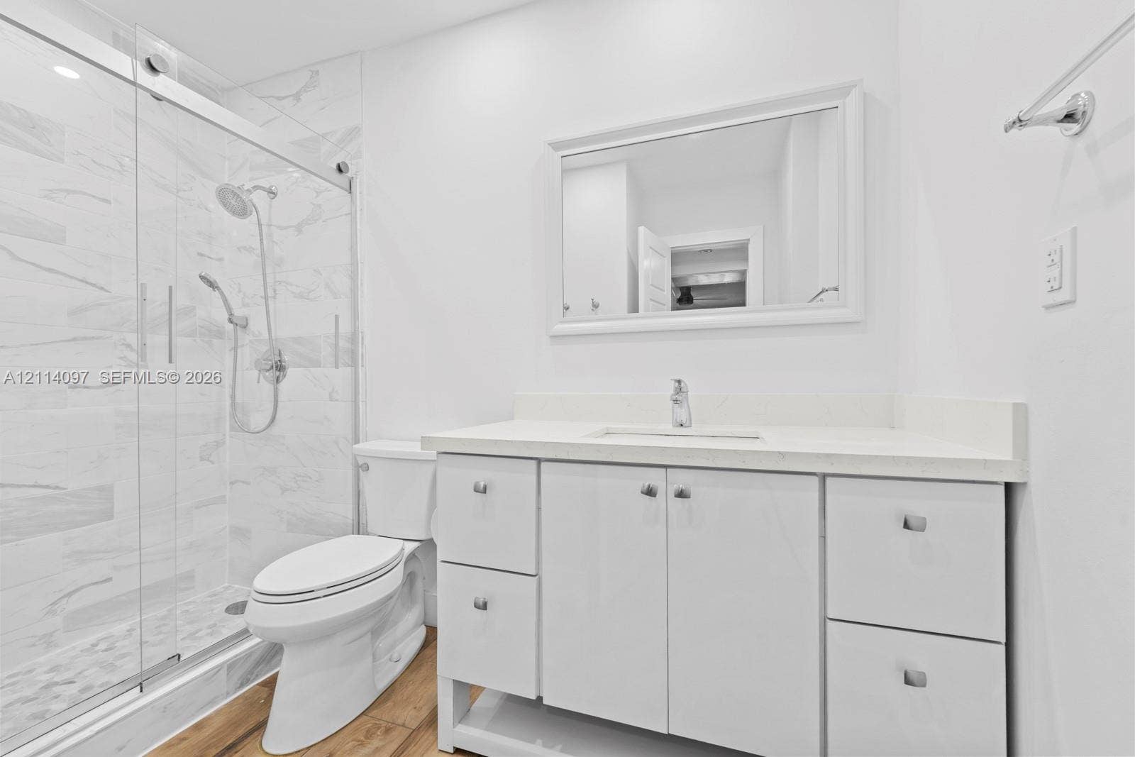 7905 SW 104th Street, #206H, Miami, FL 33156 Bathroom featuring a white vanity with integrated basin and stone-finish countertop, a glass-enclosed walk-in shower with tiled walls, and wood-finish flooring